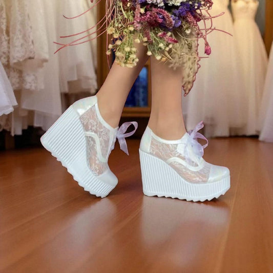 White lace-up platform shoes worn with a bouquet of flowers on a wooden floor.