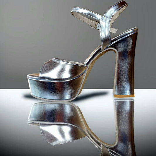 Silver high-heeled shoe on a reflective surface with a gray background