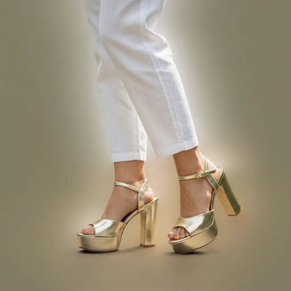 Gold high-heeled shoes worn with white pants on a neutral background