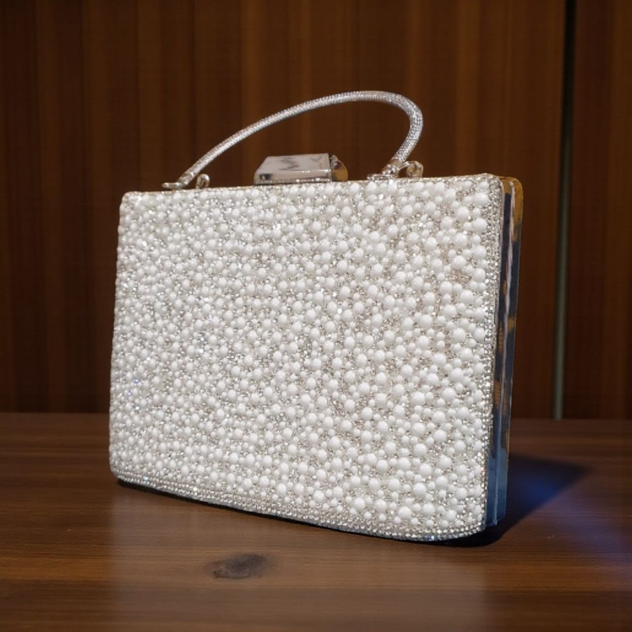 Pearl white bridal clutch with full pearl beading and metallic top handle on a wooden surface