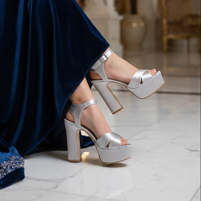 Person wearing silver high-heeled shoes and a blue dress in an elegant interior setting.