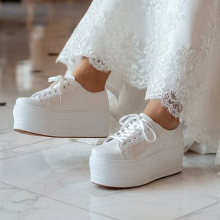 White platform sneakers worn with a white lace dress on a marble floor.