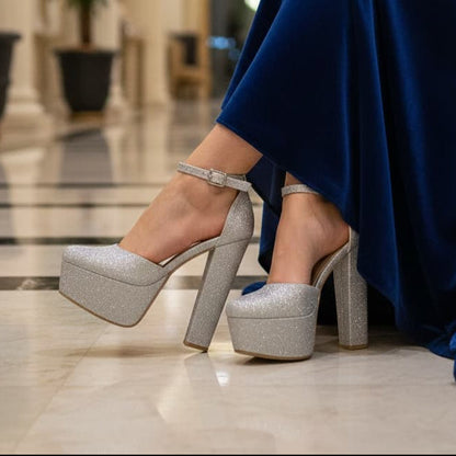 Silver glittery high-heeled shoes worn with a blue dress in an indoor setting.