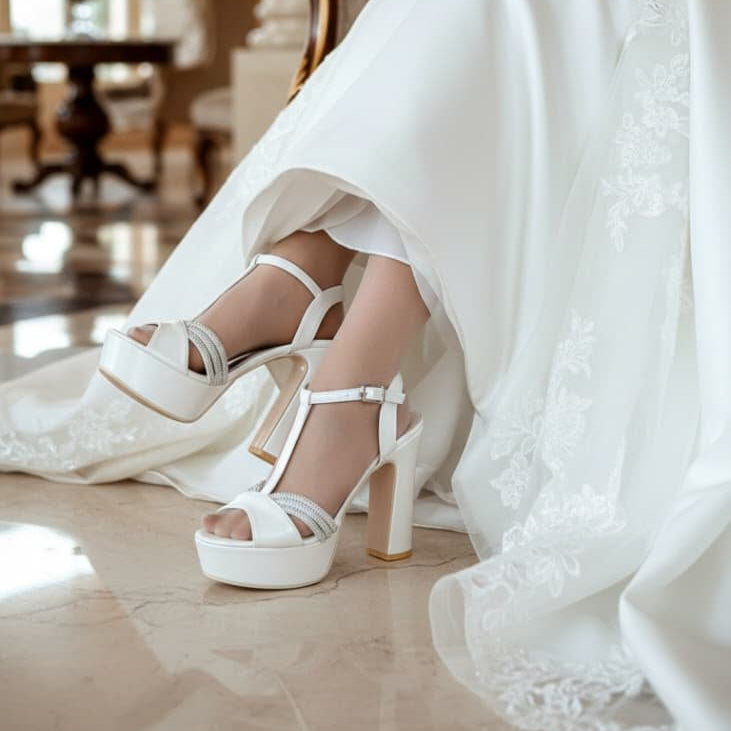 White wedding shoes with a platform and high heel worn by a person in a white dress.