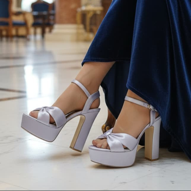 White platform high heels worn by a person in a blue dress sitting on a chair.