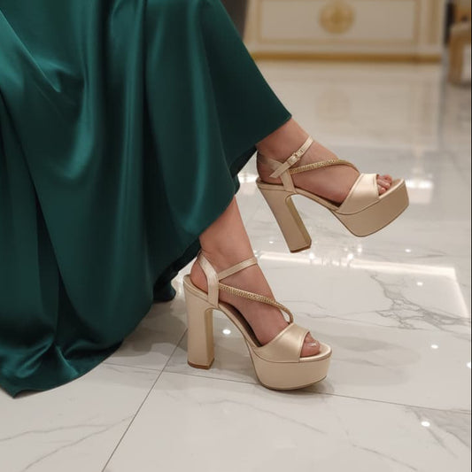 Person wearing a green dress and beige high-heeled sandals in an indoor setting.