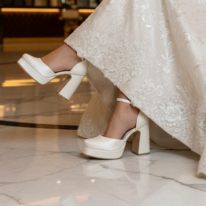White wedding shoes worn with a lace dress on a marble floor.