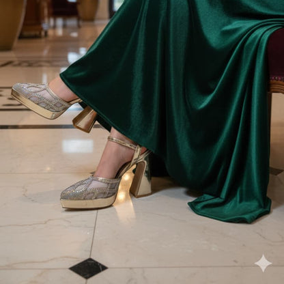 Person wearing a green dress and gold shoes in an indoor setting with a chandelier and plants.