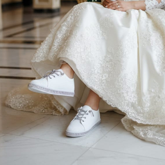 Person in a wedding dress sitting on an ornate chair holding a bouquet in a grand room.