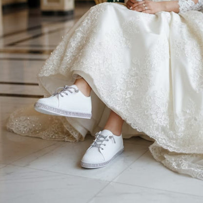 Person in a wedding dress sitting on an ornate chair holding a bouquet in a grand room.