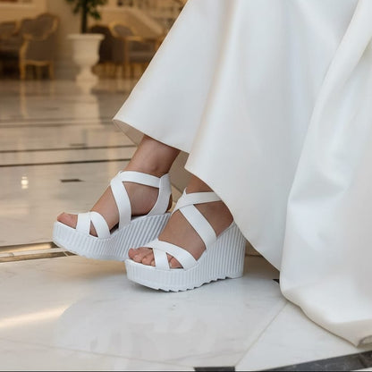 White platform sandals worn with a white dress in an elegant indoor setting.