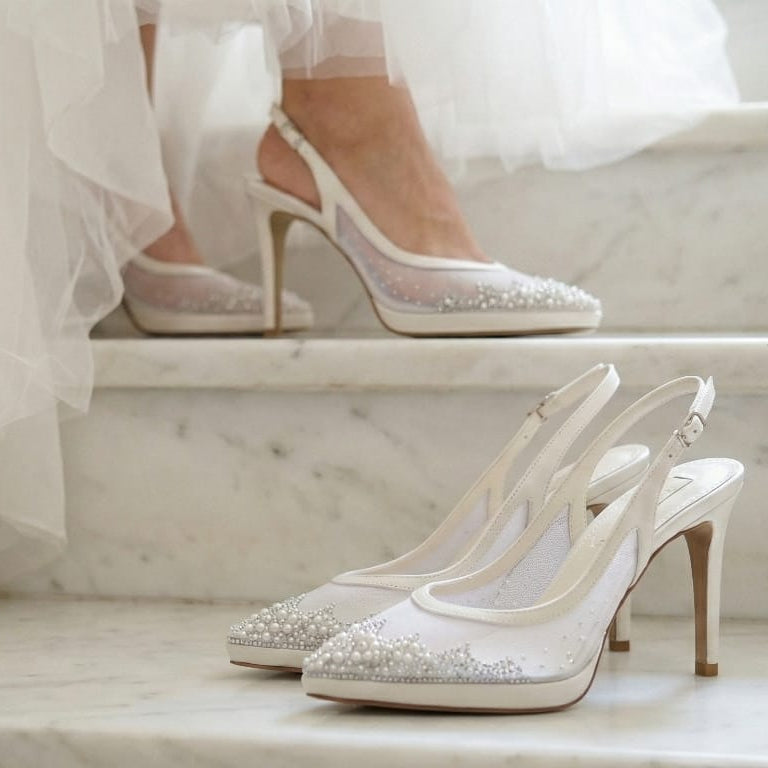 Silver high-heeled wedding shoes with sparkling details on a marble surface.