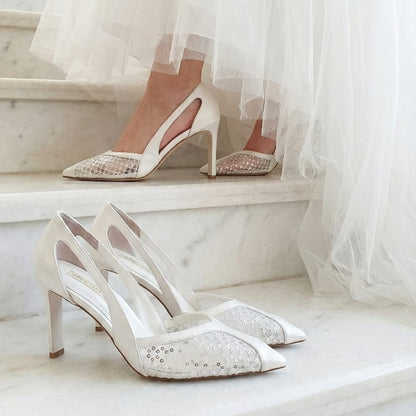 White wedding shoes with lace details on a marble surface, with a blurred background of a bride in a white dress in Lobby in Beirut.