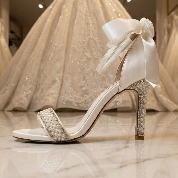 White high-heeled shoe with decorative bow in front of a wedding dress