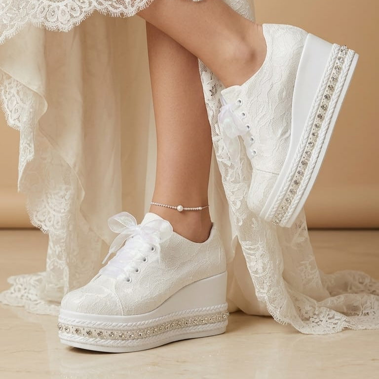 White lace-up wedge platform sneakers with embellished platform edges, shown on a model wearing a white lace dress in a warm beige setting.