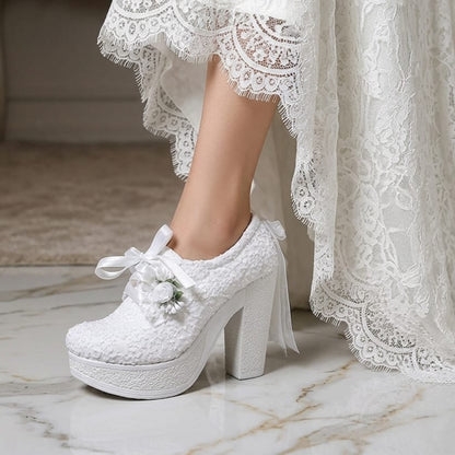 White lace bridal high-heeled shoes with decorative elements on a marble floor.