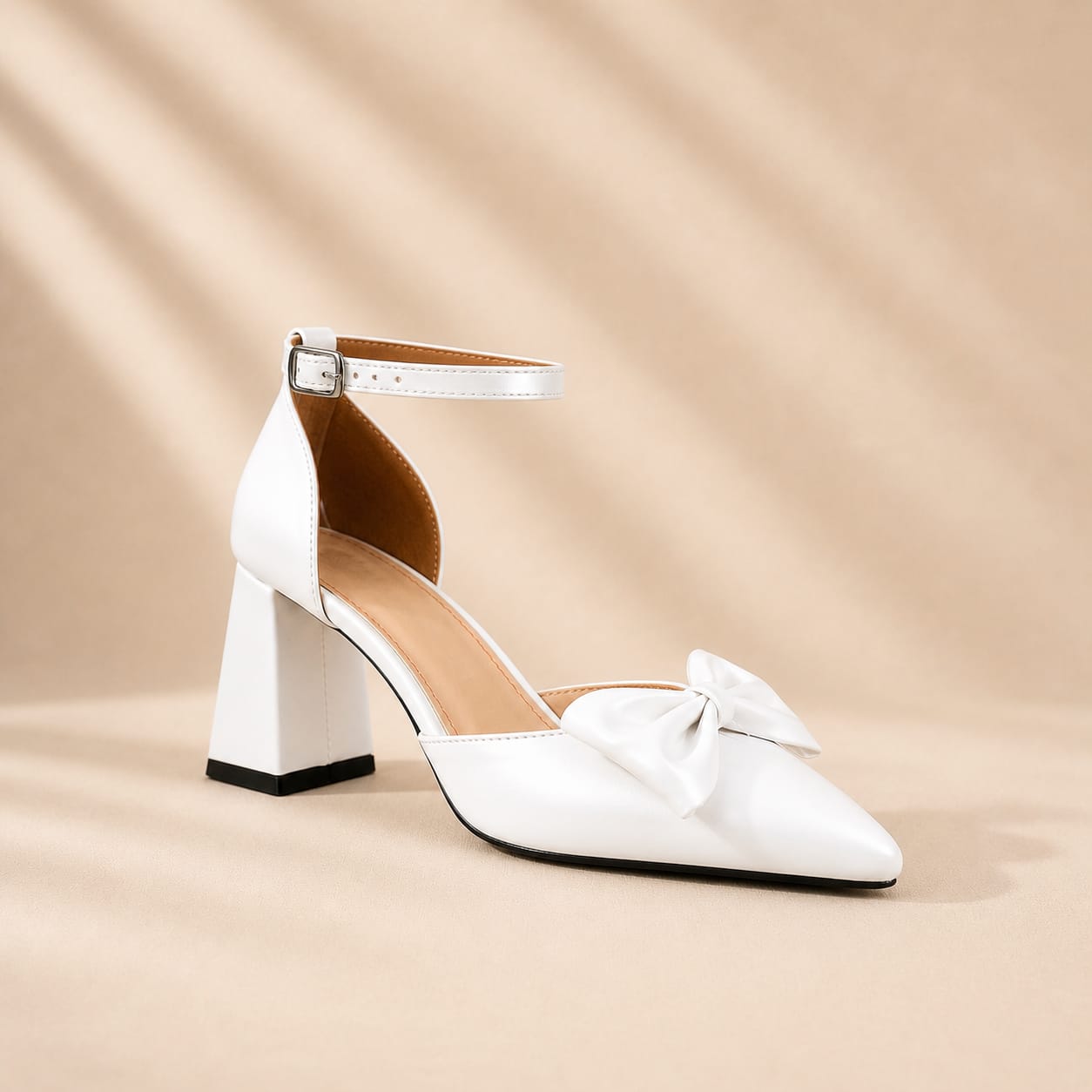 White pointed-toe bridal block heel with bow detail, ankle strap, and buckle, photographed on a beige luxury background. Elegant wedding shoes for brides, bridesmaids, graduations, first communion, baptisms, engagements, evenings, and special occasions in Beirut, Lebanon by White Lily Brides.