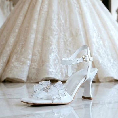White wedding dress with lace details and a matching  bridal white sandal on a marble floor.
