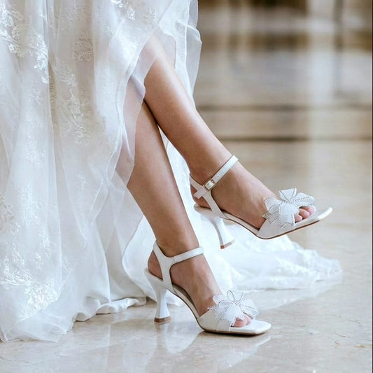 White wedding dress with lace details and white sandals on a marble floor.