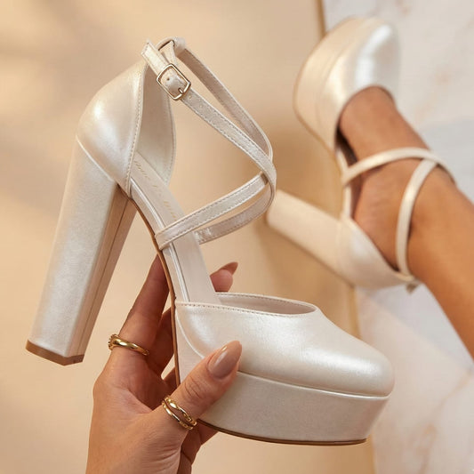 pearl White high-heeled shoes with platform sole held by a hand against a neutral background