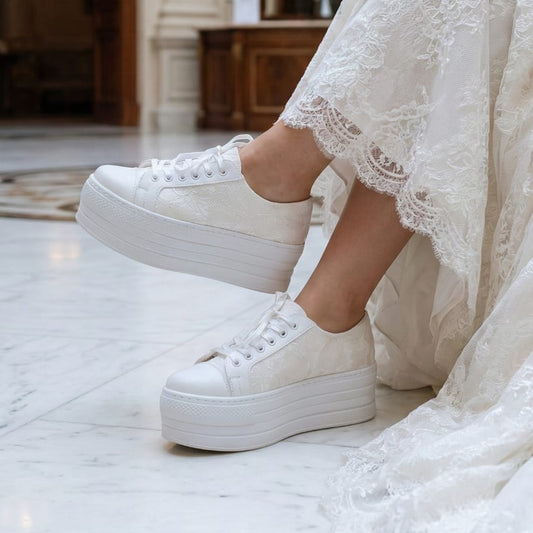 Person wearing a white lace dress and platform bridal sneakers in an elegant interior setting.
