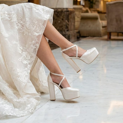 Trendy white bridal shoes with a double sole platform and chunky block heel on a polished marble floor.