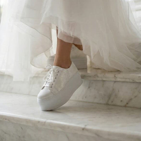 Person wearing white sneakers and a flowing white dress on marble steps.